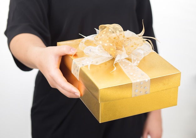 Women hands holding gold gift box. Women waring black dress on white background