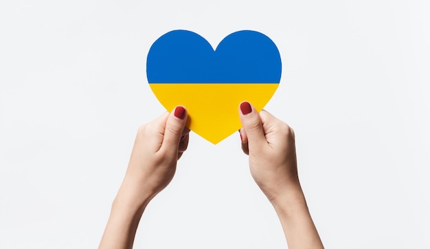 Photo women hands holding ukraine flag color heart shape paper on white background