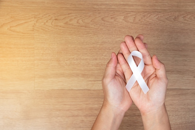 Women hands holding white bow, white ribbons on wooden background.