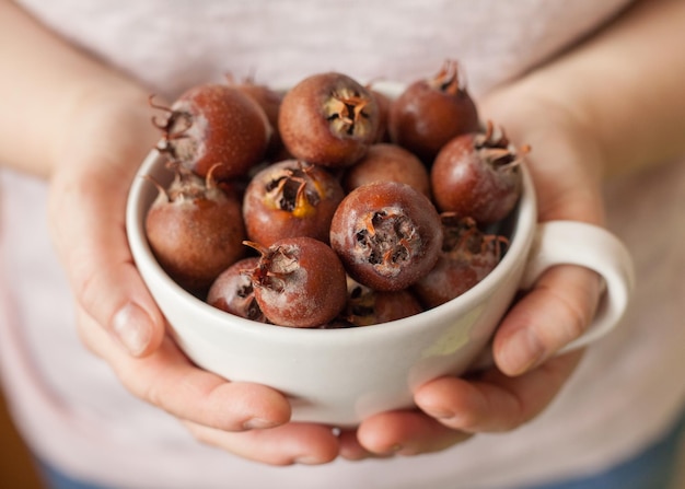 Foto le mani delle donne che tengono una ciotola bianca piena di medlar