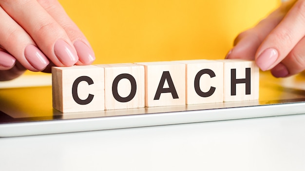 Women hands puts a wooden blocks with the letters coach on the surface of the notepad. can be used for business concept. yellow background