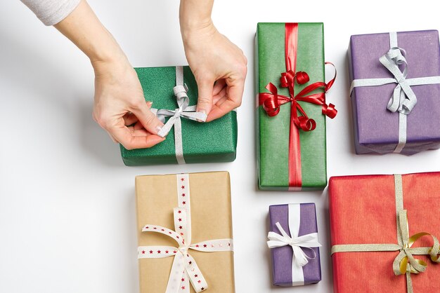 Women hands tying ribbon on green gift box on white table top view