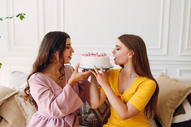 Women happy friends at home sit and eat white birthday cake.