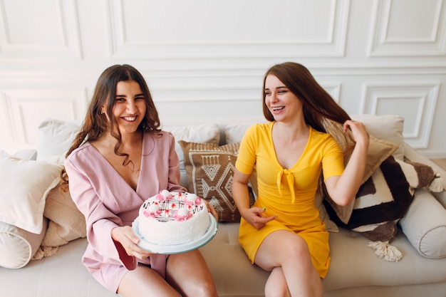 Women happy friends at home sitting and smiling with white birthday cake.