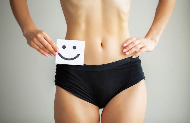 Women Health. Closeup Of Healthy Female With Beautiful Fit Slim Body In White Panties Holding White Card With Happy Smiley Face In Hands. Stomach Health And Good Digestion s