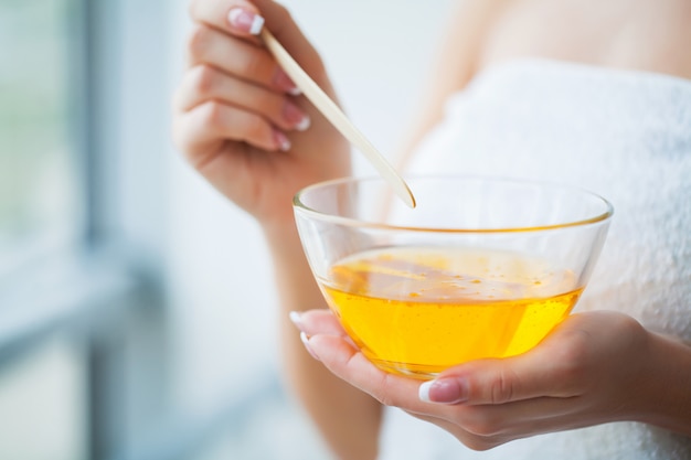 Women hold orange paraffin wax bowl. Woman in beauty salon