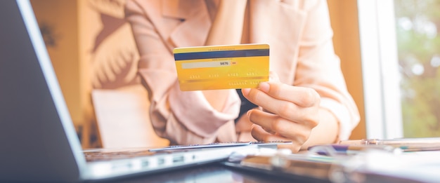 Le donne tengono tre carte di credito per fare acquisti online con un computer portatile. per banner web.