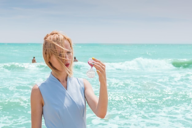 砂時計と海の背景の概念を保持している女性は夏に旅行します