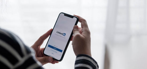 Женщина держит iPhone с приложением LinkedIn на экране. LinkedIn - приложение для обмена фотографиями для смартфонов.