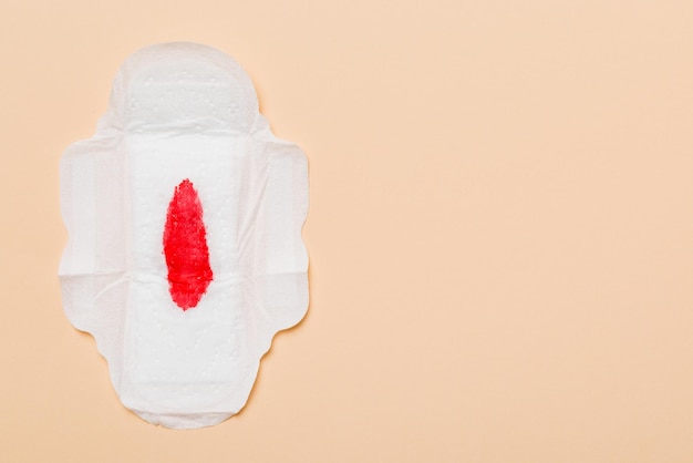 Photo women hygiene products or sanitary pad with red feather on colored background pastel color closeup empty place for text female daily hygiene