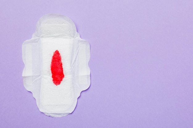 Women hygiene products or Sanitary pad with red feather on colored background Pastel color Closeup Empty place for text Female daily hygiene