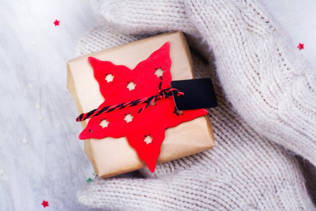 Women is holding a small gift box in hands worn in white knitted mittens