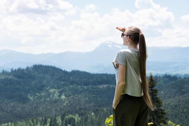 女性が立って遠くを見ています。森と山を背景に