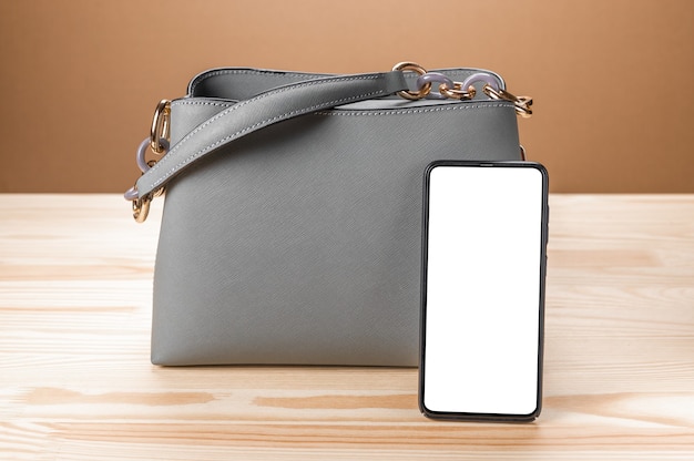 Women leather grey handbag and cell mobile smart phone with blank white screen.