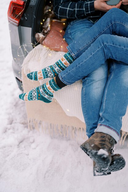 Women legs on men knees sitting on bedspreads in the trunk of a car cropped faceless