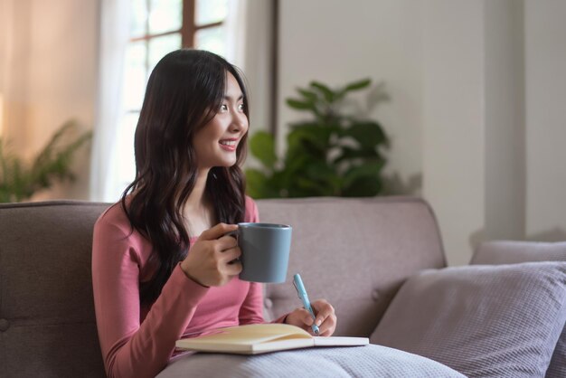 Women looking outside enjoy with dreamy while drinking tea and writing diary in lifestyle at home