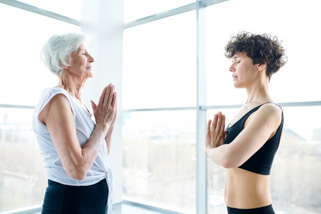 Women meditating and practicing yoga next to a large window