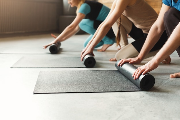 Donne e uomini che tirano fuori il tappetino da yoga e si preparano a meditare l'allenamento nella sessione di lezione di yoga con i suoi amici, copia dello spazio. concetto di stile di vita attivo e sano