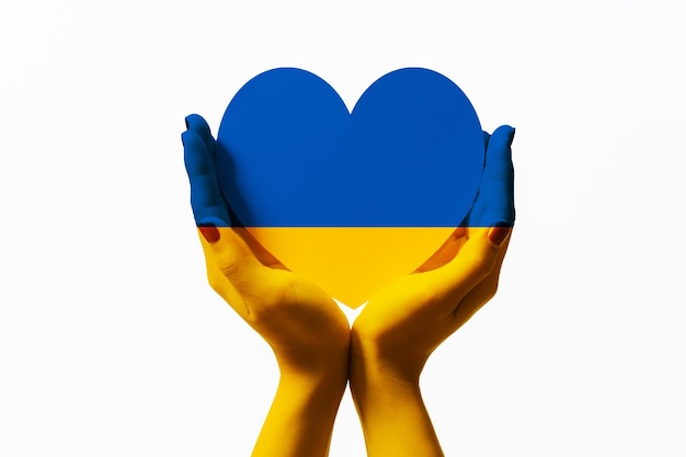 Women painted hands with the ukraine flag color holding ukraine flag color heart shape paper on white background