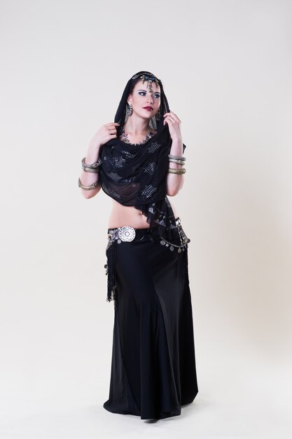 Women performs belly dance in ethnic dress on beige background, studio shot