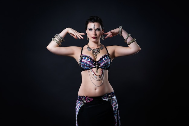 Women performs belly dance in ethnic dress on black background, studio shot