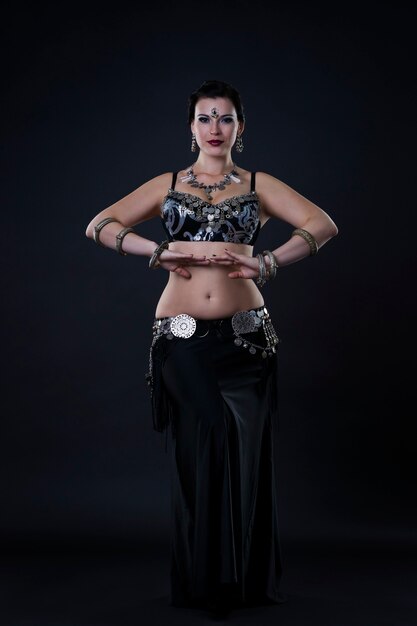 Women performs belly dance in ethnic dress on black background, studio shot