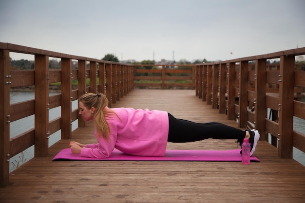women in pink hoodie doing exercises outdoors in the pier in autumn