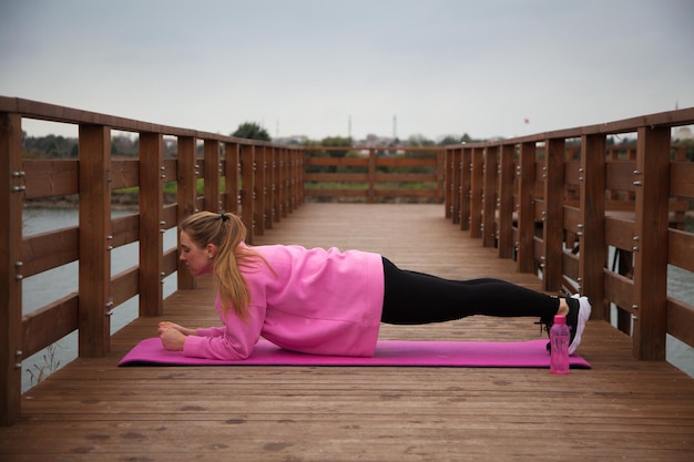 Women in pink hoodie doing exercises outdoors in the pier in autumn