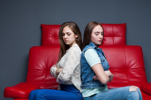 Women quarrel,two quarreling girlfriends sits on red leather couch