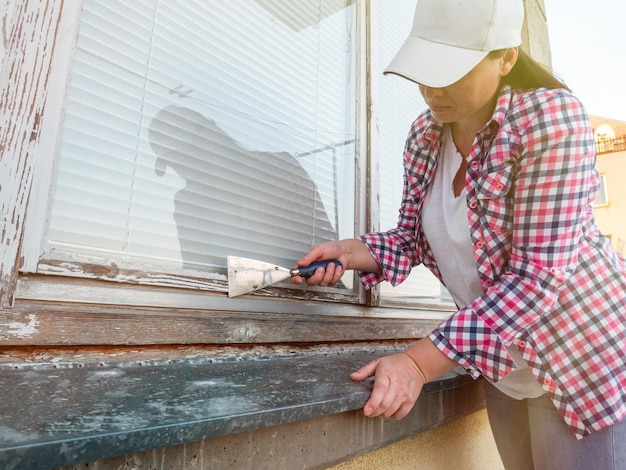 Photo women remove the old layer of paint with a wooden window using a spatula