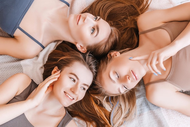 Women rest and have fun Girlfriends laugh at home lying on the floor on pillows Tree girls make homemade face and hair beauty masks Women take care of youthful skin