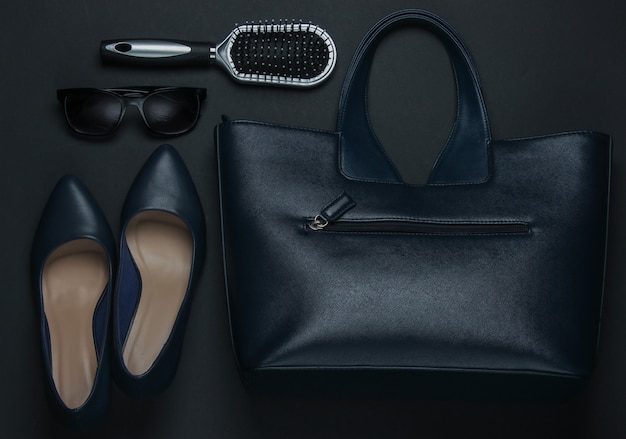 Women's accessories on a black background. High heel shoes, leather bag, comb, sunglasses. Top view