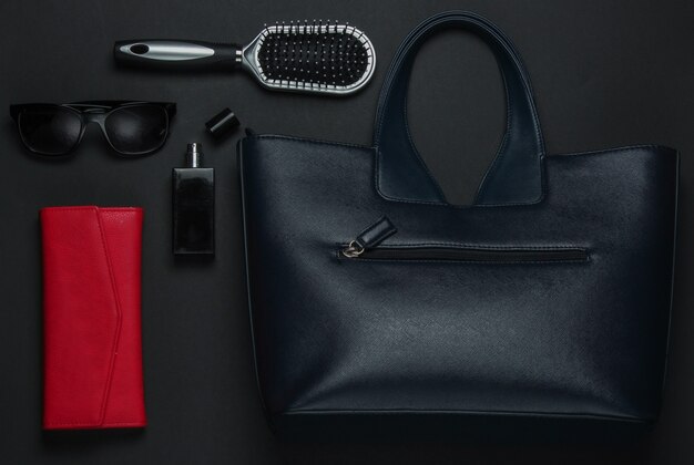 Women's accessories on a black background. Purse, leather bag, comb, sunglasses, perfume bottle. Top view