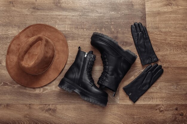 Women's accessories Black Leather boots gloves and hat on wooden floor Top view Flat lay