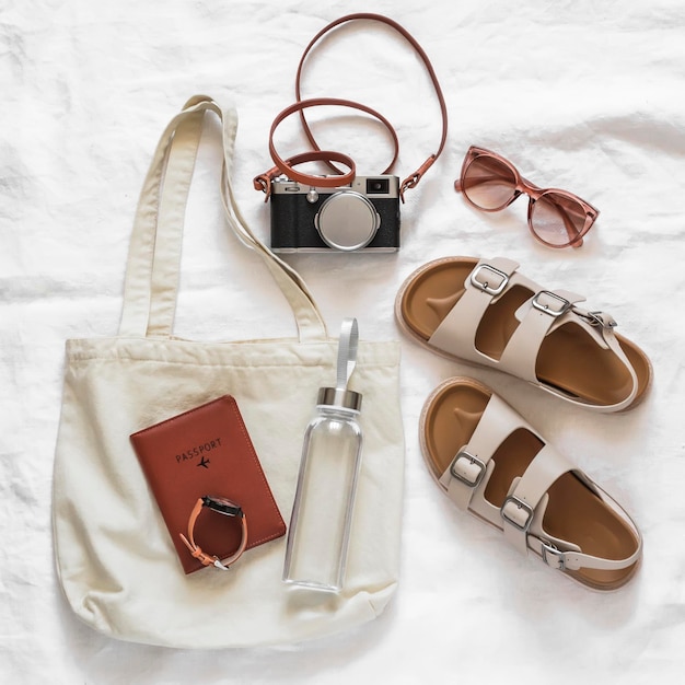 Women's accessories for comfortable rest travel canvas shopper camera comfortable leather sandals sunglasses water bottle on a light background top view