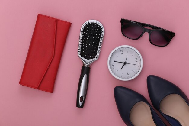 Women's accessories. High-heeled shoes, wallet, comb, sunglasses and clock on pink.