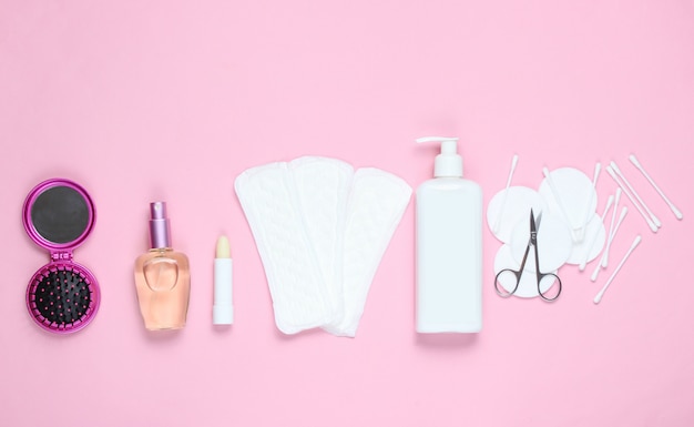 Women's beauty and hygiene products on pink pastel background. Perfume bottle, hygienic lipstick, pads, bottle cream, nail scissors.