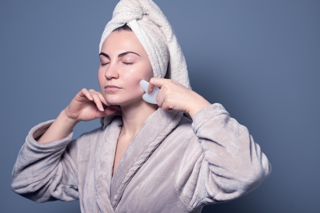 Women's beauty and spa. Beautiful woman using guasha jade stone roller massaging her face