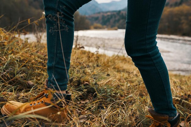 Фото Женские ноги джинсы туфли сухая трава осенняя река горы на расстоянии фото высокого качества