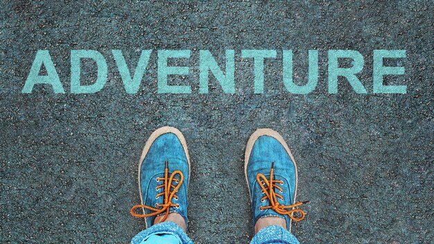 Women's feet in sneakers stand at the line with the inscription adventure.