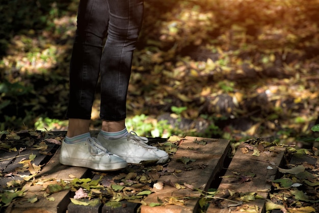 Women's feet in white sneakers on a wooden bridge Autumn park on a background