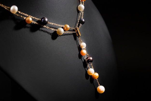 Women's gold necklace made of chains and pearls on a black stand. Close-up