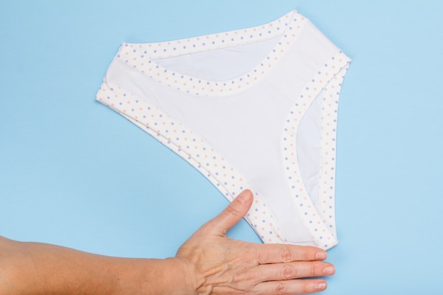 Women's hand holding beautiful cotton panties on blue background.