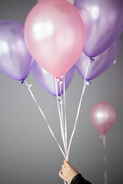 Women's hand holding helium balloons in pink and purple