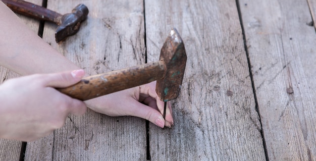 Women's hand is keep hammer and to drive a nail is lying on a black wooden table.