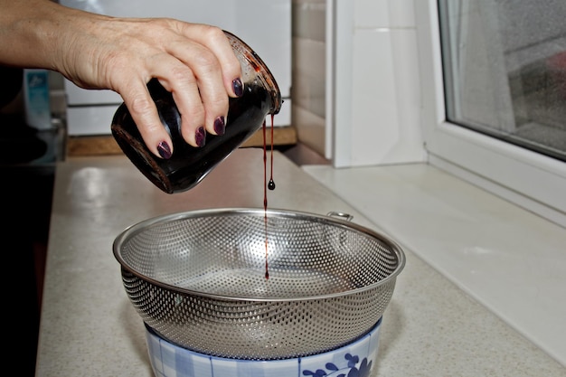 Фото Женские руки заливают варенье из банки в миску через сито на фоне кухни интерьера выпечки приготовления пищи