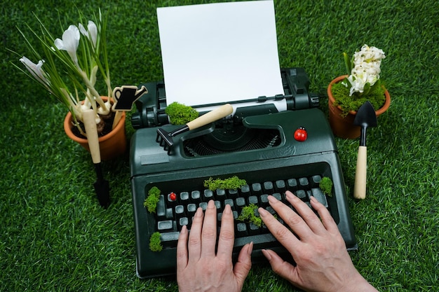 Фото Женские руки печатают на зеленой пишущей машинке, поросшей мхом. креативное фото.