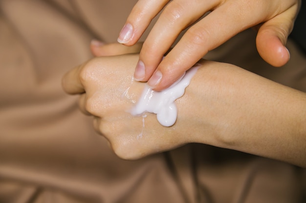 Foto mani delle donne su uno sfondo di tessuto beige una donna spalma la crema sulle mani. prodotto cosmetico. cura e cura della pelle.