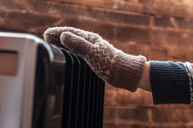 Photo women's hands in christmas, warm, winter mittens on the heater. keep warm in the winter, cold evenings. heating season