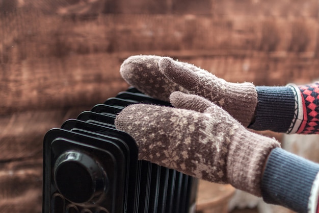 Photo women's hands in christmas, warm, winter mittens on the heater. keep warm in the winter, cold evenings. heating season